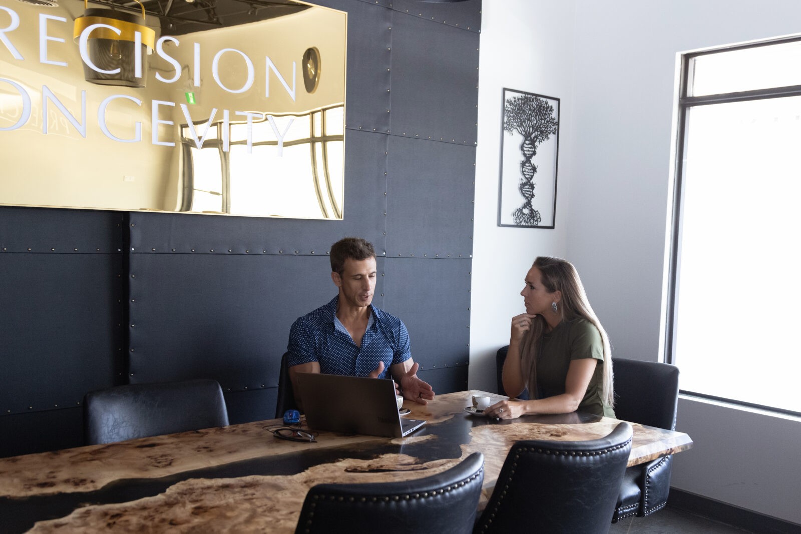 A man and a woman at a large desk looking at a laptop