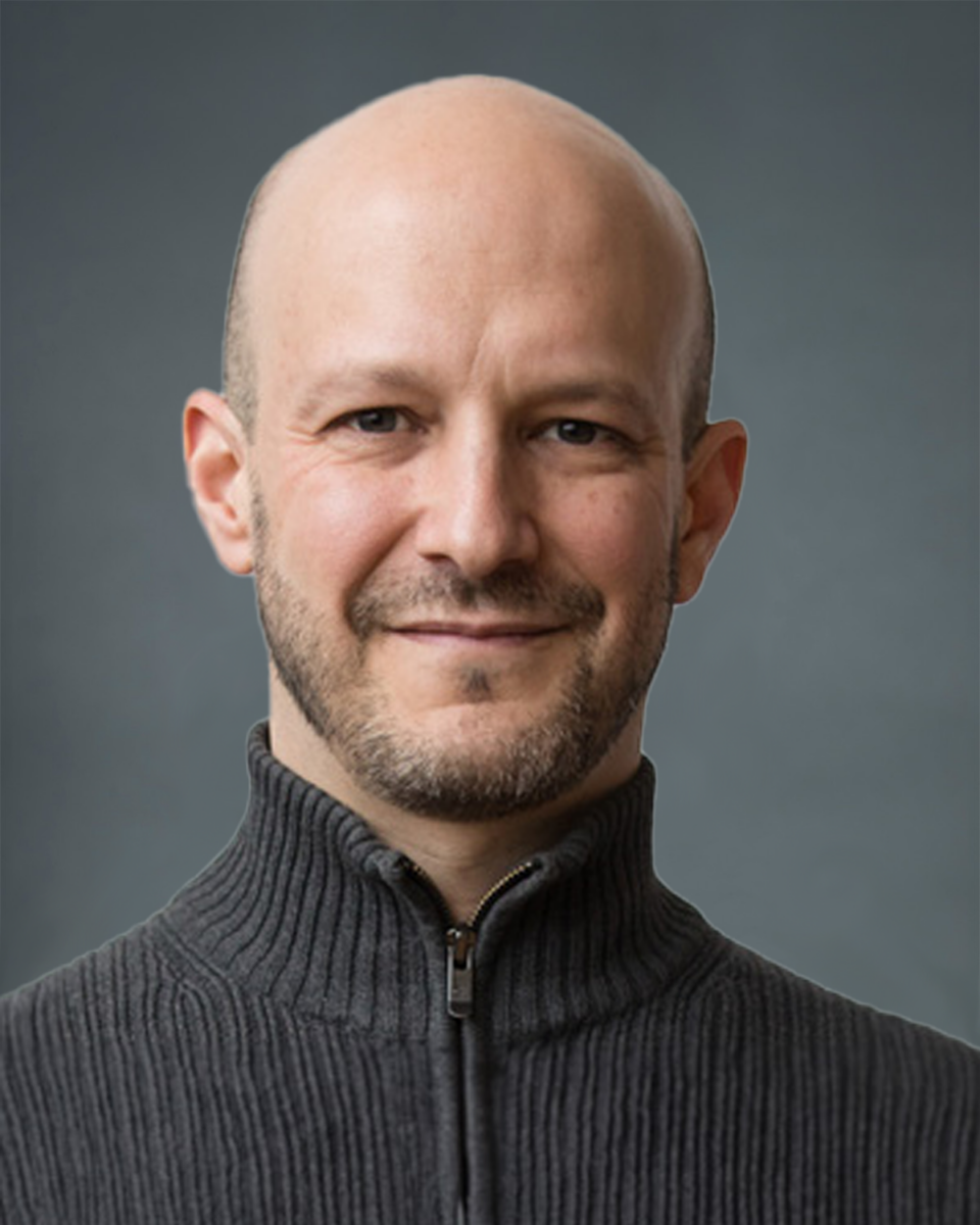 A bald man in a gray sweater smiles for the camera.